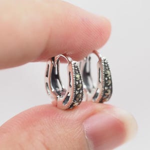 May include: A pair of silver hoop earrings with a row of small, dark gray gemstones around the edge.