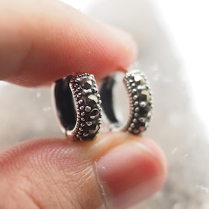 Könnte beinhalten: Ein Paar silberne Creolen mit einer Reihe schwarzer Markasit-Steine um den Reifen.