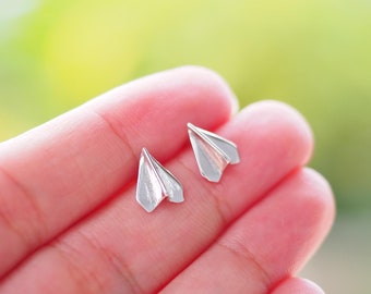 May include: A pair of silver paper airplane earrings. The earrings are small and delicate, and they are perfect for adding a touch of whimsy to any outfit.