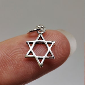 Può includere: Un piccolo ciondolo a forma di Stella di David color argento. Il ciondolo è una stella a sei punte con spazi aperti tra le punte. Ha un piccolo anello nella parte superiore per attaccarlo a una collana o un braccialetto. Il ciondolo è tenuto da un dito.