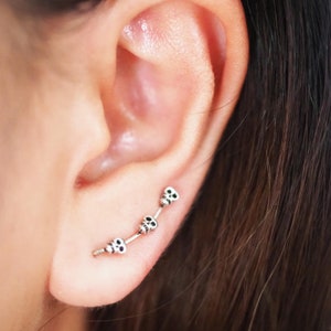 May include: A silver ear cuff with four small skull charms. The cuff is curved and sits on the upper part of the ear.
