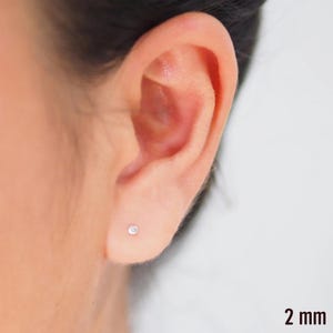 May include: A close-up of a person's ear with a small, silver stud earring. The earring is 2 mm in diameter.