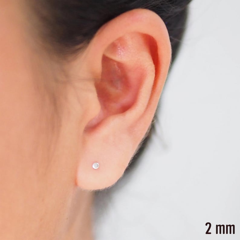 May include: A close-up of a person's ear with a small, silver stud earring. The earring is 2 mm in diameter.
