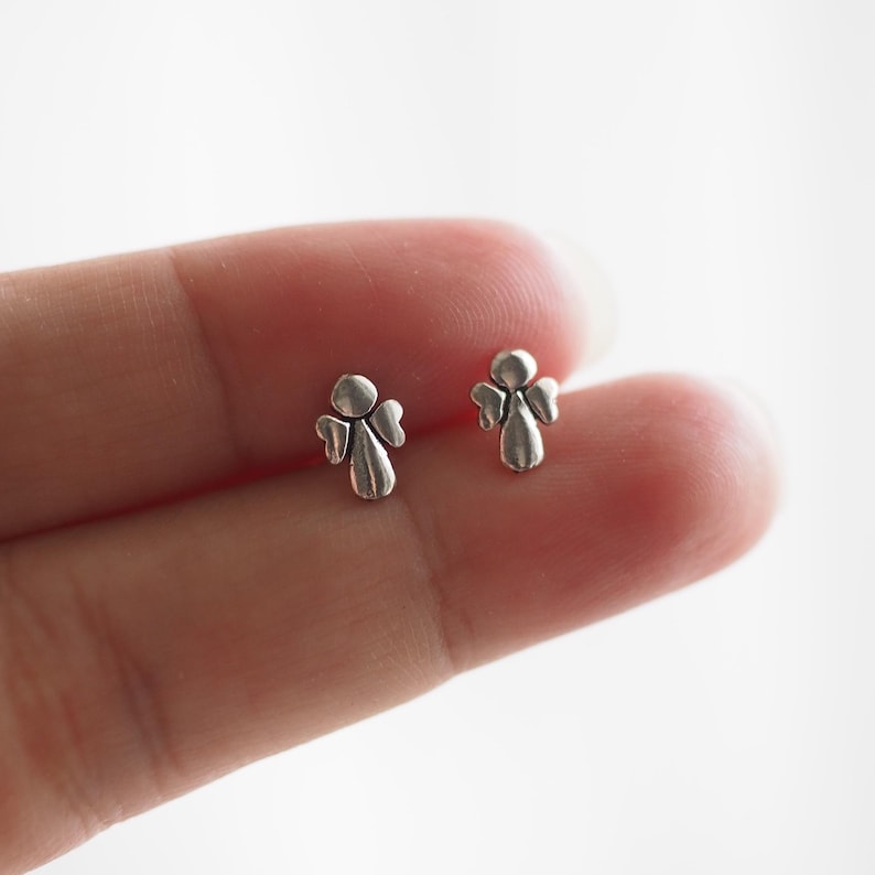 K&ouml;nnte beinhalten: Ein Paar silberne Engels-Ohrstecker. Die Engel sind klein und detailliert, mit Fl&uuml;geln und einem Heiligenschein.