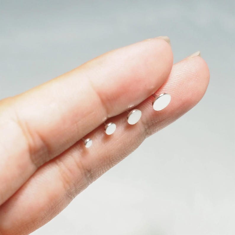 May include: Four silver disc earrings of varying sizes, displayed on a finger.