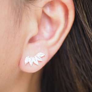 May include: A silver ear climber earring with five clear, marquise-cut cubic zirconia stones. The stones are arranged in a curved, ascending pattern, creating a sparkling, elegant look. The earring is shown on an ear.