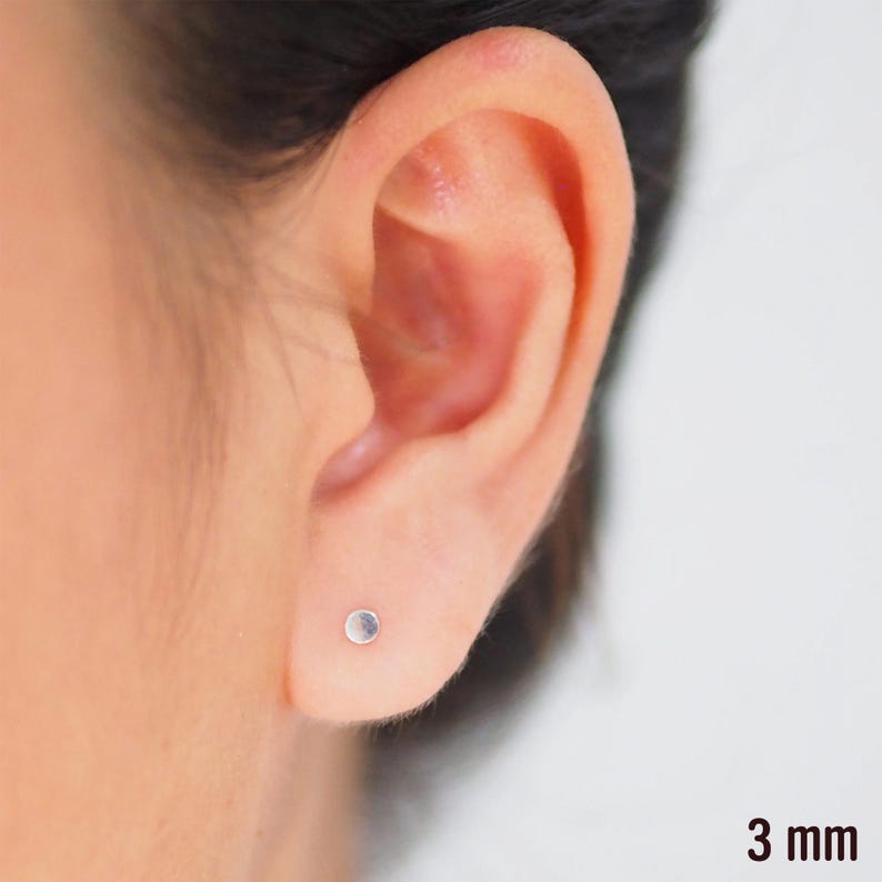 May include: A close-up of a person's ear with a small, silver stud earring. The earring is 3 mm in diameter.