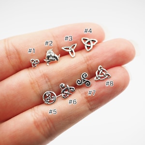 May include: Eight silver Celtic knot designs, numbered 1 through 8, are displayed on a hand. The knots are small and intricate.