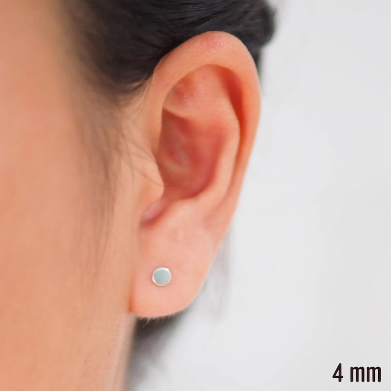 May include: A close-up of a person's ear with a small, round, silver stud earring. The earring is 4 mm in diameter.