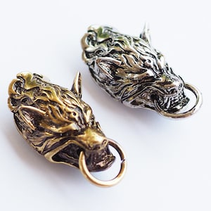 May include: Two wolf head belt buckles, one silver and one gold, with a detailed design and a ring on the side.