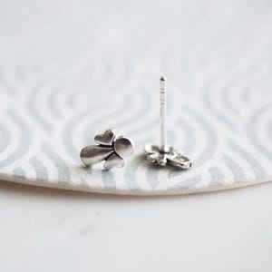 K&ouml;nnte beinhalten: Ein Paar silberne Ohrstecker in Engelform. Die Ohrringe sind klein und zart, mit einem schlichten Design.