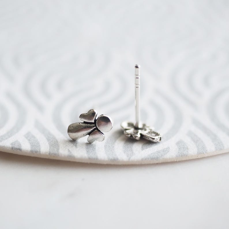 K&ouml;nnte beinhalten: Ein Paar silberne Ohrstecker in Engelform. Die Ohrringe sind klein und zart, mit einem schlichten Design.