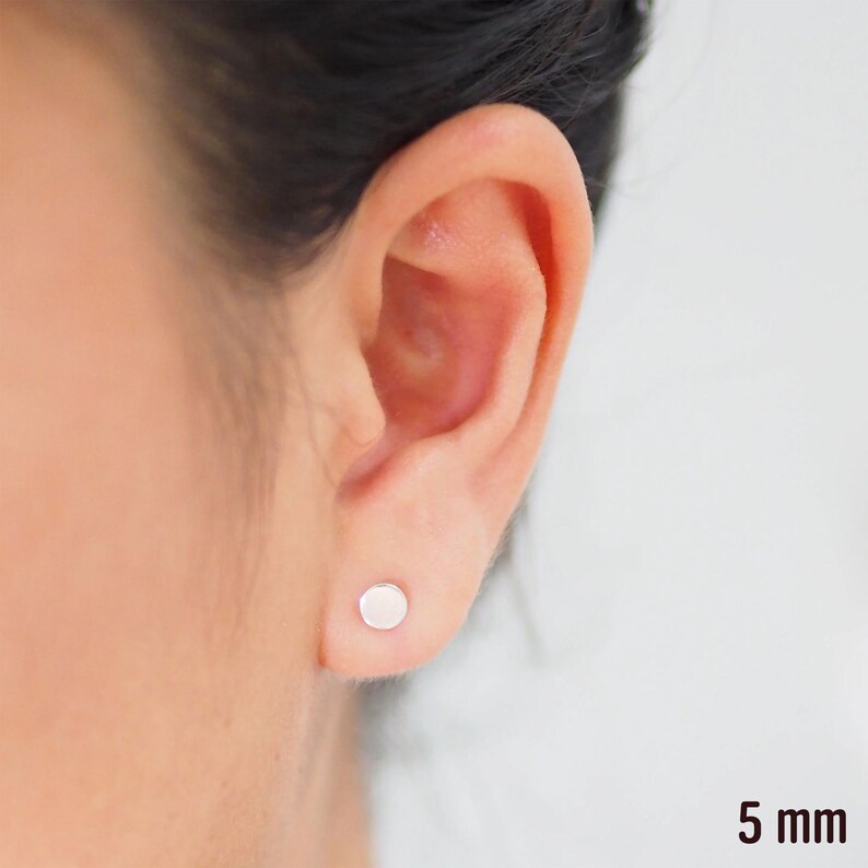 May include: A close-up of a person's ear with a small, round, silver stud earring. The earring is 5 mm in diameter.