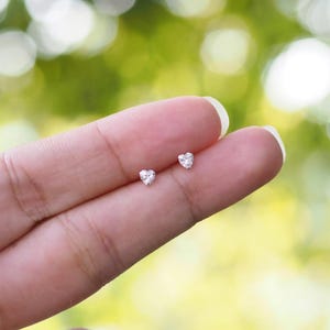 May include: A pair of small, silver heart-shaped earrings with clear cubic zirconia stones.