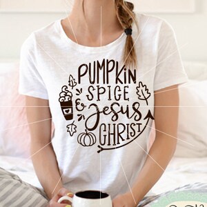 May include: A white tote bag with the text "Pumpkin Spice & Jesus Christ" in brown lettering. The text is surrounded by a pumpkin, leaves, and a cup of coffee. The bag has the word "SAMPLE" printed on the bottom.