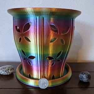 Puede incluir: Una maceta impresa en 3D con un diseño de hojas decorativas en colores arcoíris. La maceta tiene un platillo de drenaje.