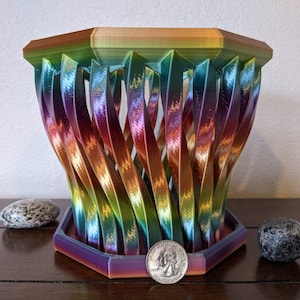 Op de afbeelding: Een regenboogkleurige, 3D-geprinte, achthoekige plantenpot met een gedraaid ontwerp. De pot is gemaakt van plastic en heeft een gladde, glanzende afwerking.