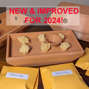 May include: Three terracotta-colored 3D printed trays with a small terracotta-colored funnel in the center tray. The trays are filled with small yellow sponges. Three yellow envelopes with the text "Mason Clay" are on a wooden surface. The text "NEW & IMPROVED FOR 2024!" is in red text at the top of the image.