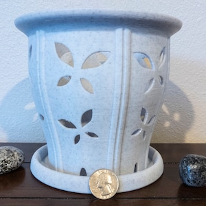 Op de afbeelding: Witte keramische plantenpot met een decoratief bladmotief en een schotel. De pot heeft een gespikkelde afwerking en is ontworpen om een ​​kleine plant te houden.