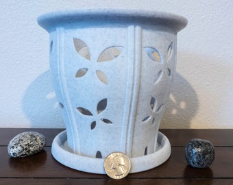 May include: White ceramic planter with a decorative leaf pattern and a saucer. The planter has a speckled finish and is designed to hold a small plant.