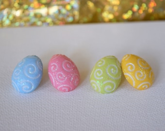 Könnte beinhalten: Vier dekorative Ostereier mit einem Wirbelmuster. Die Eier sind hellblau, rosa, grün und gelb.