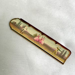 May include: A rectangular folding fan featuring a dark brown frame and a decorative panel depicting three scenes of figures in pink dresses and green outfits dancing in a landscape with trees under a light sky, with scalloped edges along the top.