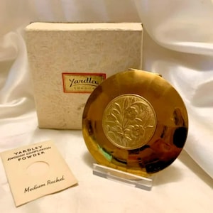 May include: A gold compact mirror with an engraved floral design. The mirror is in its original box, which is white with black lettering that reads "Yardley English Complexion Powder" and "Medium Rachel".