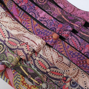 May include: A collection of colourful patterned elastic bands with a glittery finish. The bands are arranged in a stack, with the top band being a light brown with a gold glitter finish. The other bands are a mix of purple, pink, and black with various patterns.