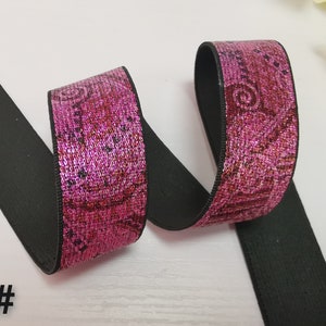 May include: Pink elastic trim with a black backing. The trim has a metallic sheen and a floral pattern.