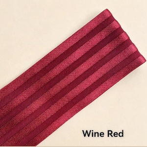 Peut inclure: Une bande de tissu &eacute;lastique rouge vin pr&eacute;sentant une s&eacute;rie de cr&ecirc;tes verticales parall&egrave;les et sur&eacute;lev&eacute;es sur toute sa longueur. Le mat&eacute;riau a un &eacute;clat subtil et une surface textur&eacute;e, avec le texte Wine Red imprim&eacute; en noir dans le coin.