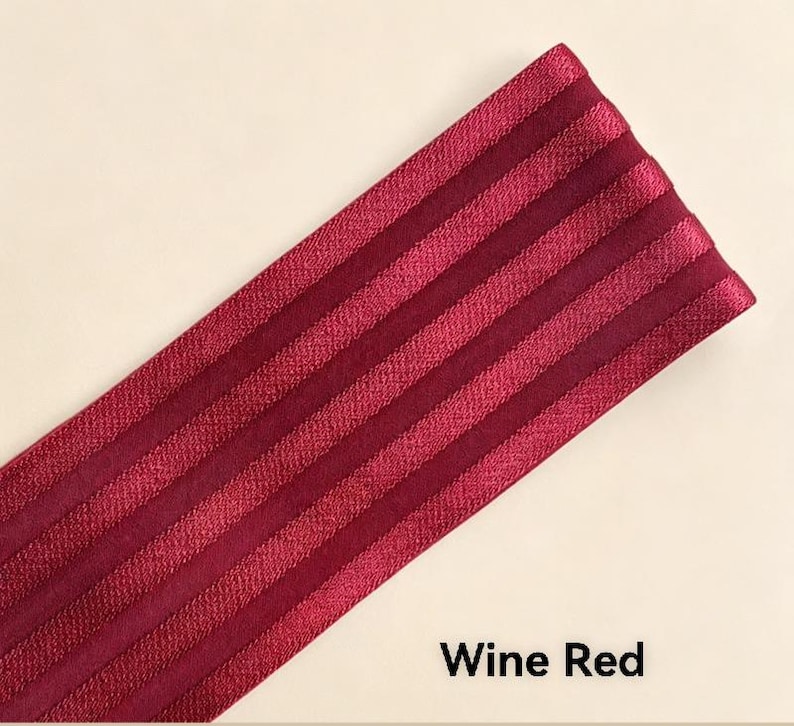 Peut inclure: Une bande de tissu &eacute;lastique rouge vin pr&eacute;sentant une s&eacute;rie de cr&ecirc;tes verticales parall&egrave;les et sur&eacute;lev&eacute;es sur toute sa longueur. Le mat&eacute;riau a un &eacute;clat subtil et une surface textur&eacute;e, avec le texte Wine Red imprim&eacute; en noir dans le coin.
