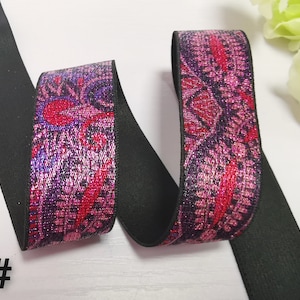 May include: Black elastic with a pink and purple floral pattern with silver glitter accents. The elastic is folded in half and the pattern is visible on both sides.