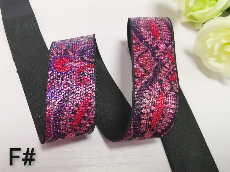 May include: Black elastic with a pink and purple floral pattern with silver glitter accents. The elastic is folded in half and the pattern is visible on both sides.