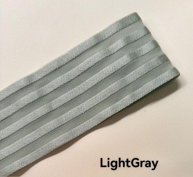 Peut inclure: Une bande de tissu &eacute;lastique gris clair pr&eacute;sentant une s&eacute;rie de rayures diagonales en relief parall&egrave;les sur sa surface. Le mat&eacute;riau a une texture lisse et l&eacute;g&egrave;rement r&eacute;fl&eacute;chissante, avec le texte LightGray inscrit en bas &agrave; droite.