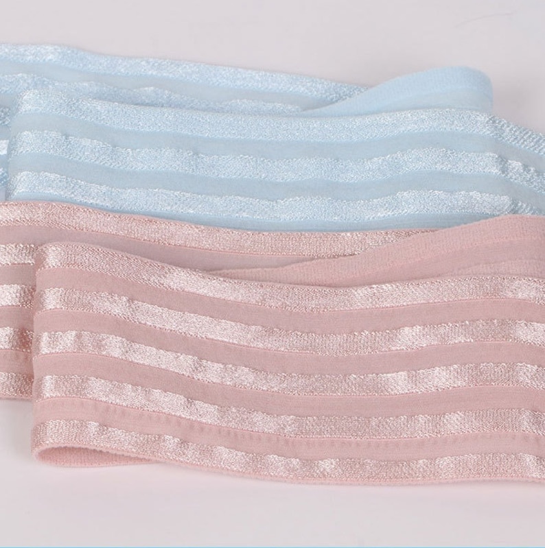 Peut inclure: Deux bandes de tissu &eacute;lastique, une bleu clair et une rose poudr&eacute;. Chaque bande pr&eacute;sente un motif r&eacute;p&eacute;titif de rayures horizontales l&eacute;g&egrave;rement en relief, avec un aspect m&eacute;tallique scintillant sur toute la longueur du mat&eacute;riau.