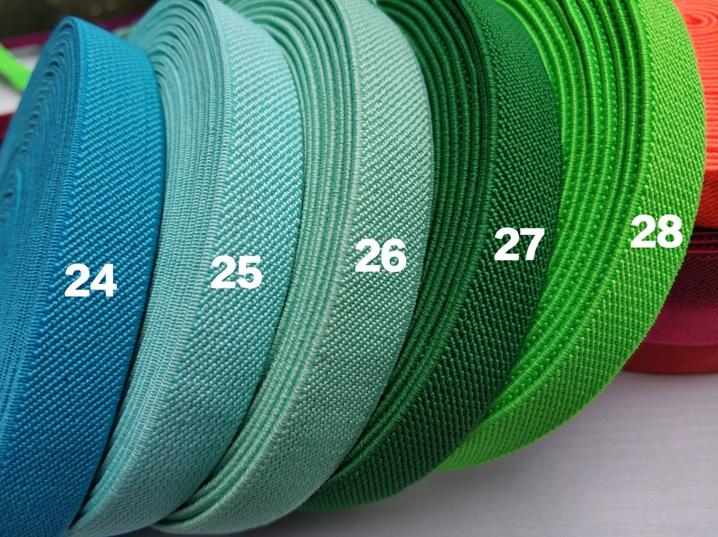 May include: Five rolls of elastic fabric in different shades of blue and green. The rolls are labeled with the numbers 24, 25, 26, 27, and 28.