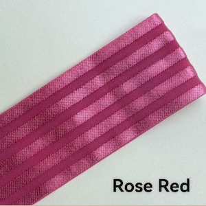 Peut inclure: Une bande de tissu &eacute;lastique rouge rose pr&eacute;sentant une s&eacute;rie de rayures parall&egrave;les, en relief et satin&eacute;es, dispos&eacute;es en diagonale sur le mat&eacute;riau. La texture alterne entre des finitions mates et brillantes, cr&eacute;ant un aspect c&ocirc;tel&eacute; distinct.