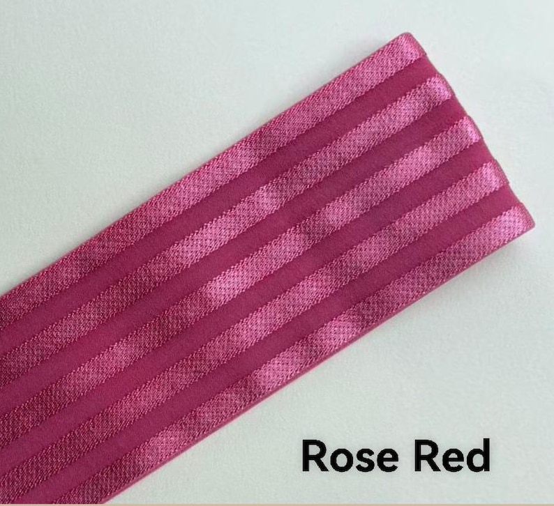 Peut inclure: Une bande de tissu &eacute;lastique rouge rose pr&eacute;sentant une s&eacute;rie de rayures parall&egrave;les, en relief et satin&eacute;es, dispos&eacute;es en diagonale sur le mat&eacute;riau. La texture alterne entre des finitions mates et brillantes, cr&eacute;ant un aspect c&ocirc;tel&eacute; distinct.