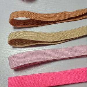May include: Four different colors of elastic ribbon, including brown, beige, pink, and bright pink. The ribbon is flat and has a textured surface.