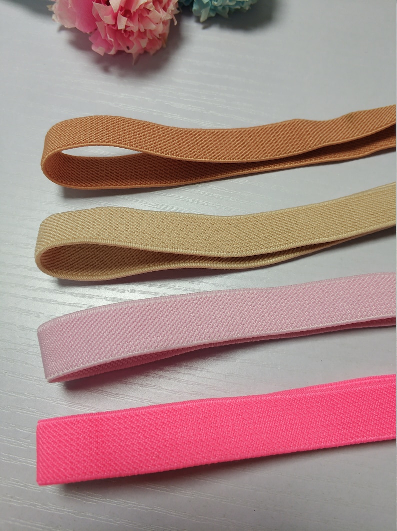 May include: Four different colors of elastic ribbon, including brown, beige, pink, and bright pink. The ribbon is flat and has a textured surface.