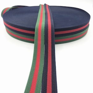 Könnte beinhalten: Zwei Rollen elastisches Band in Marineblau mit roten und grünen Streifen. Das Band ist aufgerollt und die Enden hängen herunter.