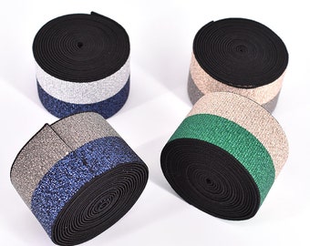 Può includere: Quattro rotoli di elastico nero con una striscia glitterata. Le strisce sono argento, oro, verde e blu.