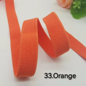 May include: A close-up of a bright orange elastic band with a textured surface. The band is folded and twisted, showing its flexibility. The text "33.Orange" is visible in the lower right corner of the image.