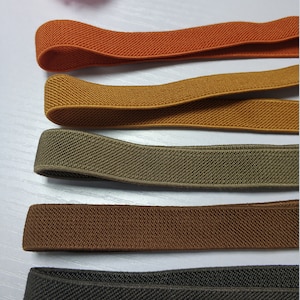 May include: Five different colors of elastic fabric, including orange, mustard yellow, olive green, brown, and black. The fabric is woven with a textured pattern.