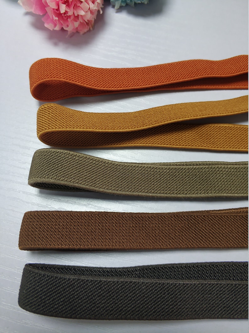 May include: Five different colors of elastic fabric, including orange, mustard yellow, olive green, brown, and black. The fabric is woven with a textured pattern.
