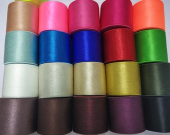 Puede incluir: Una colección de 18 carretes de cinta de satén en varios colores, incluyendo beige, rosa, rojo, naranja, azul, verde, dorado y negro.