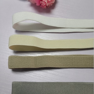 May include: Four different colors of elastic band, white, beige, brown, and gray. The elastic bands are laid out on a light wood surface.