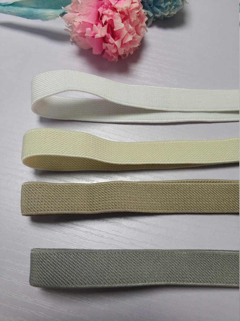 May include: Four different colors of elastic band, white, beige, brown, and gray. The elastic bands are laid out on a light wood surface.