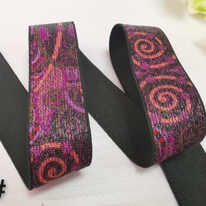 May include: Black elastic with a pink and orange patterned design. The pattern features swirls and abstract shapes. The elastic is folded in half, showing both sides of the pattern.