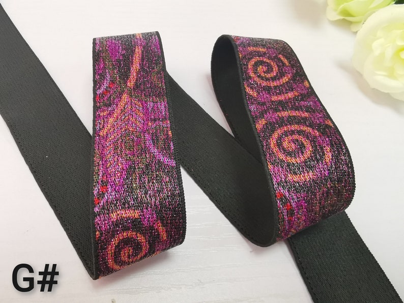 May include: Black elastic with a pink and orange patterned design. The pattern features swirls and abstract shapes. The elastic is folded in half, showing both sides of the pattern.